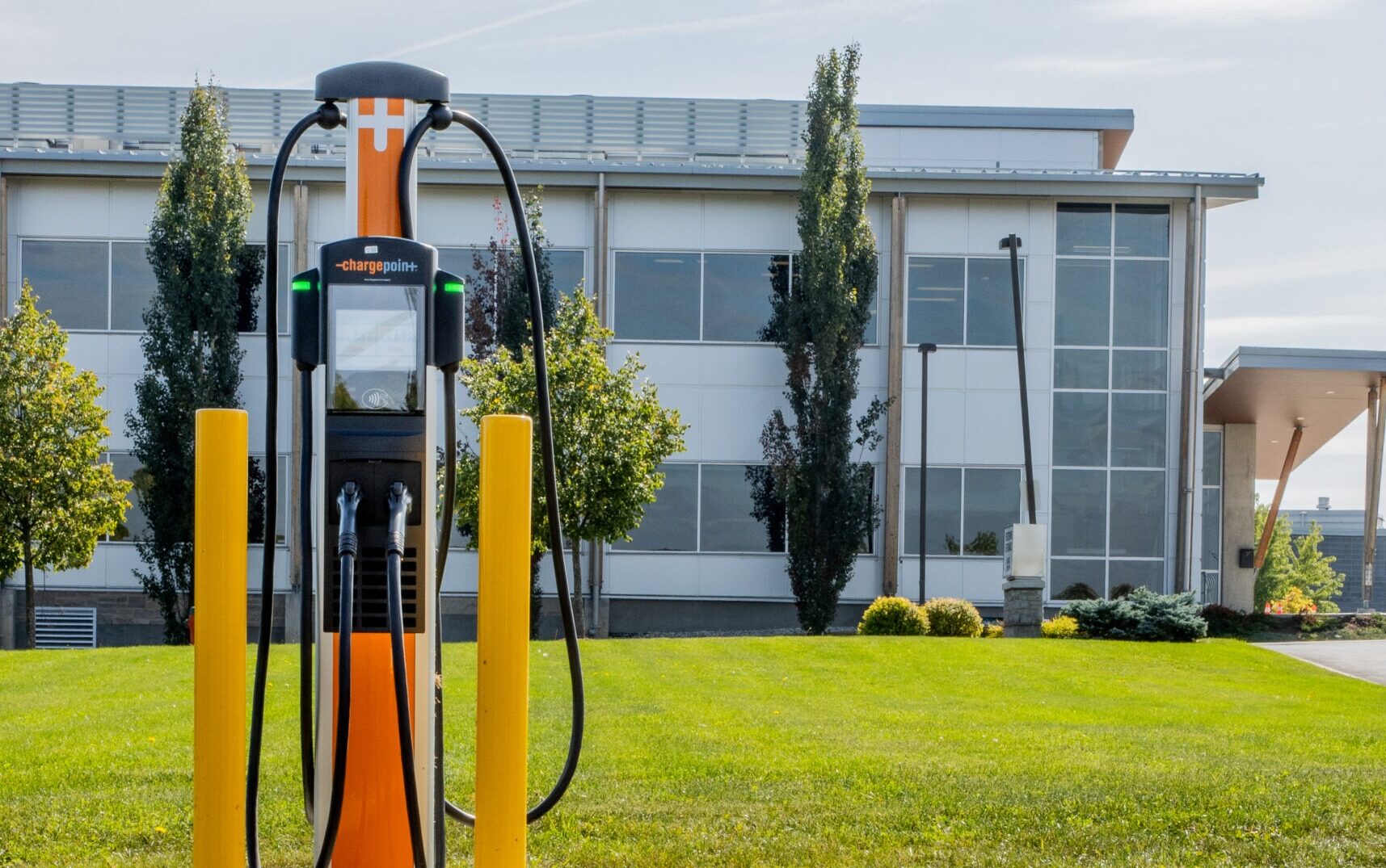 Chargepoint electric vehicle charger in front of a two-story steel and glass commercial building with a grass lawn, decorative trees and shrubs in Guelph Ontario.